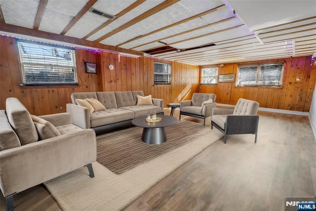 living area featuring visible vents, wooden walls, baseboards, and wood finished floors