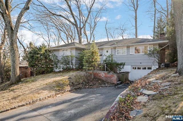 single story home featuring aphalt driveway, a chimney, an attached garage, and central air condition unit