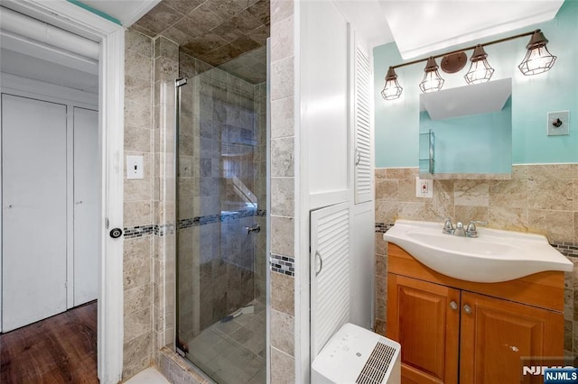 full bath featuring a stall shower, wood finished floors, vanity, and tile walls