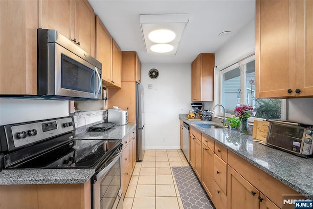 kitchen with light tile patterned floors, stainless steel appliances, a sink, baseboards, and dark stone countertops