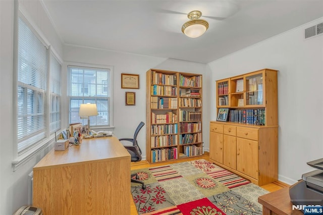 home office featuring light wood-style flooring, visible vents, and ornamental molding