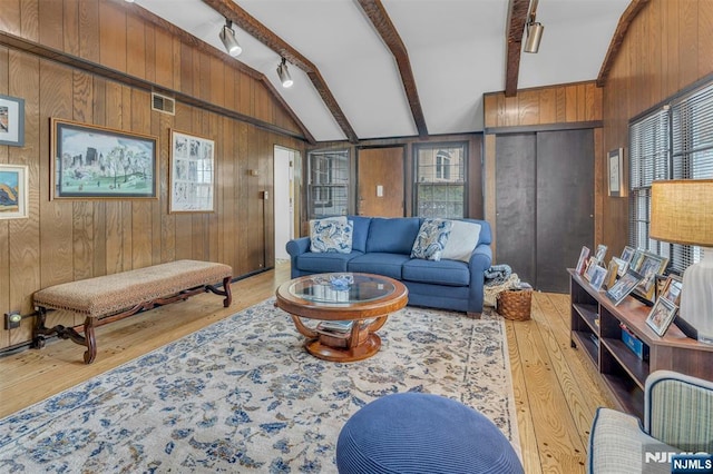 living area with light wood finished floors, visible vents, lofted ceiling with beams, wood walls, and track lighting