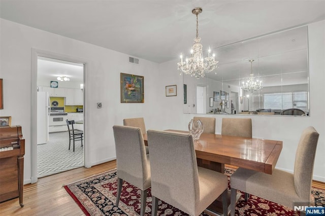 dining space featuring an inviting chandelier, baseboards, visible vents, and light wood finished floors