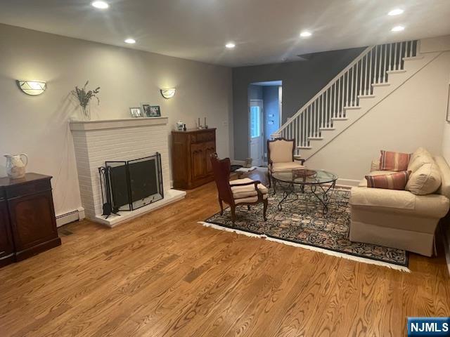 living room featuring a brick fireplace, wood-type flooring, and baseboard heating