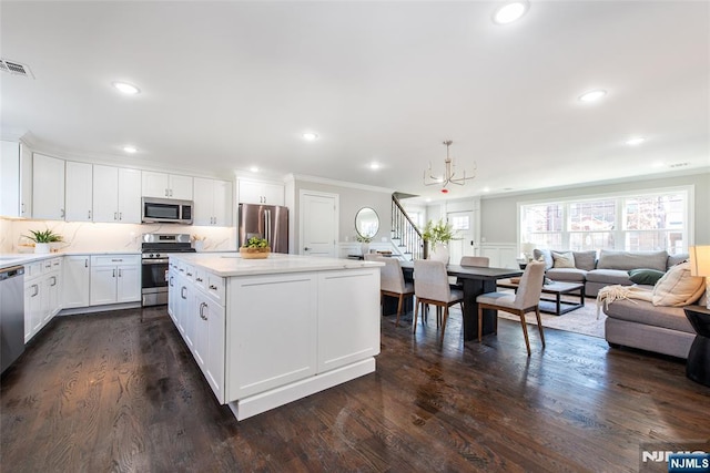 kitchen with dark wood-type flooring, decorative light fixtures, a center island, stainless steel appliances, and white cabinets