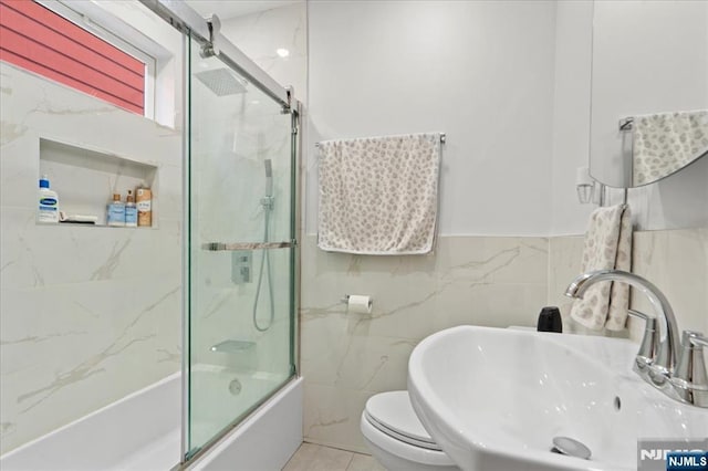 full bathroom with combined bath / shower with glass door, sink, tile walls, tile patterned flooring, and toilet