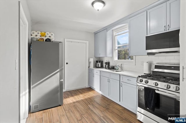 kitchen with tasteful backsplash, appliances with stainless steel finishes, sink, and wood-type flooring