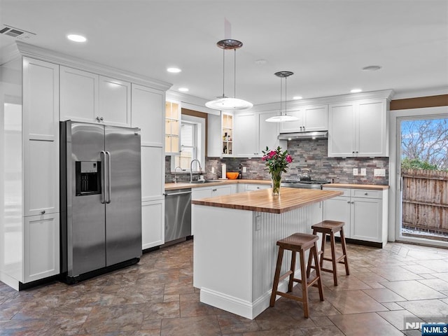 kitchen with appliances with stainless steel finishes, pendant lighting, white cabinetry, wooden counters, and a center island