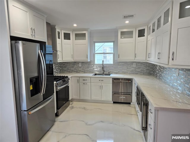 kitchen featuring sink, appliances with stainless steel finishes, white cabinetry, light stone countertops, and decorative backsplash