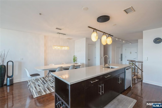 kitchen with dark wood-type flooring, stainless steel dishwasher, decorative light fixtures, sink, and a kitchen island with sink