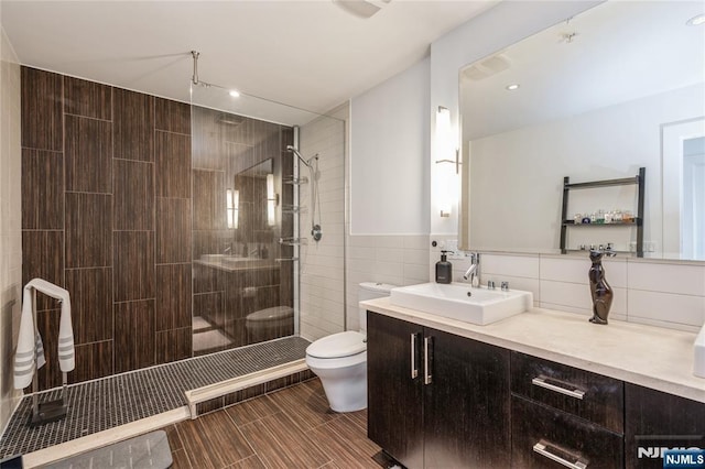 bathroom featuring toilet, tile walls, tiled shower, and vanity