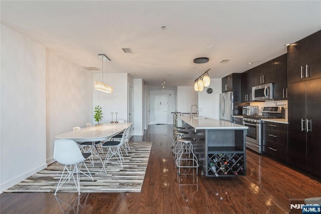 kitchen featuring a center island with sink, a breakfast bar, stainless steel appliances, hanging light fixtures, and dark brown cabinets