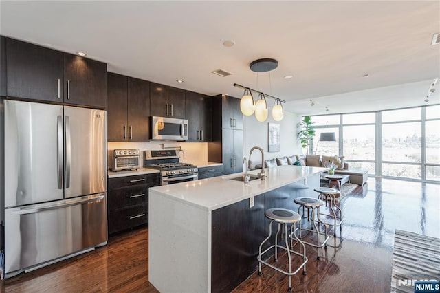 kitchen featuring a center island with sink, decorative light fixtures, sink, appliances with stainless steel finishes, and a kitchen bar