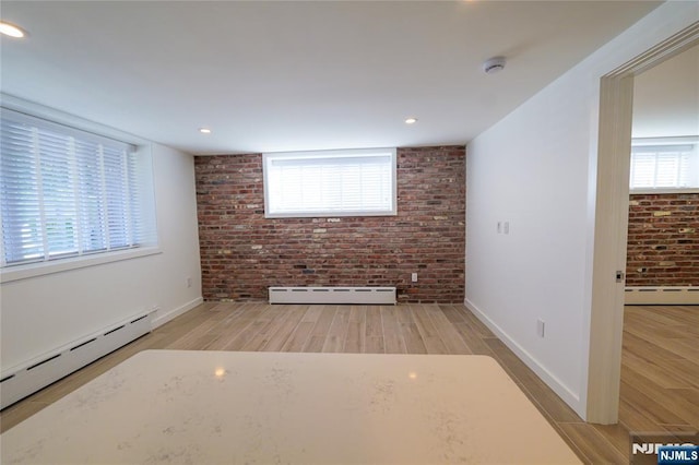 unfurnished living room with a wealth of natural light, light hardwood / wood-style floors, brick wall, and baseboard heating