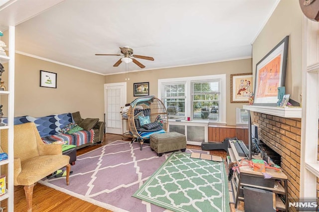 living area with hardwood / wood-style floors, crown molding, a brick fireplace, and ceiling fan