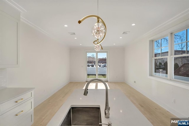 kitchen with crown molding, light hardwood / wood-style flooring, a notable chandelier, pendant lighting, and white cabinets