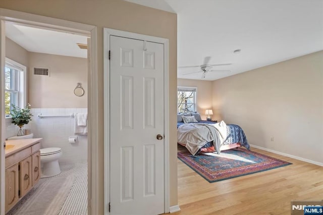 bedroom featuring ceiling fan, ensuite bathroom, tile walls, and light wood-type flooring