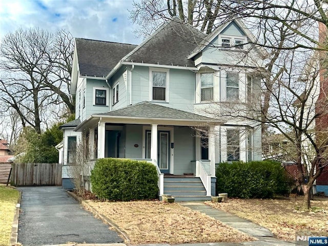 victorian home with fence, covered porch, and a shingled roof