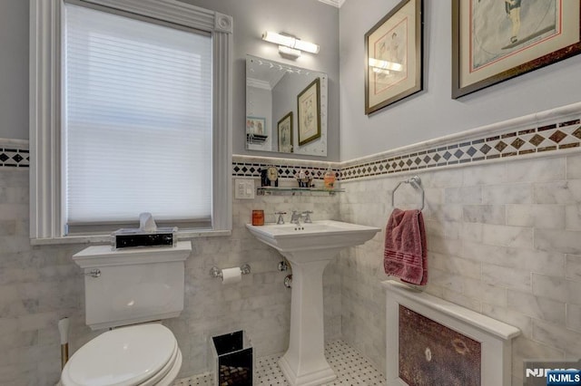 bathroom with a wainscoted wall, toilet, tile walls, and a sink