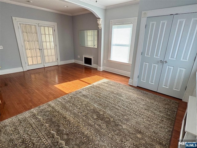 unfurnished living room featuring baseboards, wood finished floors, arched walkways, and ornamental molding