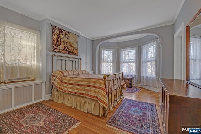 bedroom with light wood finished floors, radiator heating unit, arched walkways, and crown molding