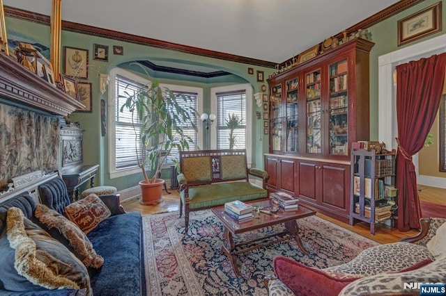 sitting room featuring arched walkways, wood finished floors, baseboards, and ornamental molding