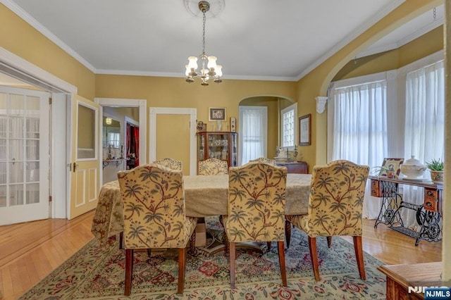 dining room with arched walkways, a notable chandelier, light wood-style floors, and ornamental molding