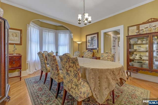 dining room with light wood finished floors, baseboards, ornamental molding, an inviting chandelier, and arched walkways