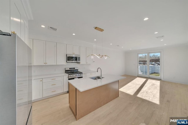 kitchen with white cabinetry, sink, hanging light fixtures, stainless steel appliances, and a center island with sink