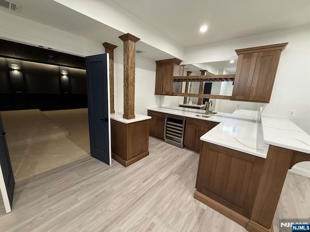 kitchen featuring decorative columns, wine cooler, a kitchen breakfast bar, kitchen peninsula, and light wood-type flooring