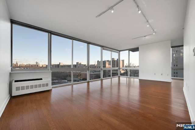 empty room with expansive windows, radiator heating unit, and hardwood / wood-style floors