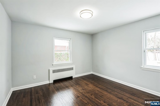 spare room featuring radiator, a wealth of natural light, and dark hardwood / wood-style flooring