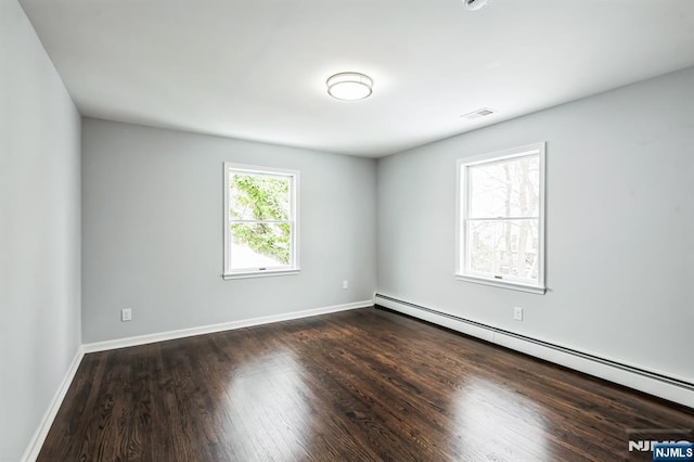 spare room featuring baseboard heating and dark hardwood / wood-style floors