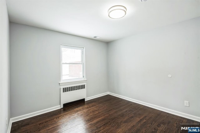 empty room featuring radiator and dark hardwood / wood-style flooring