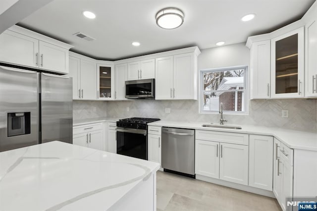 kitchen with stainless steel appliances, white cabinetry, sink, and light stone counters