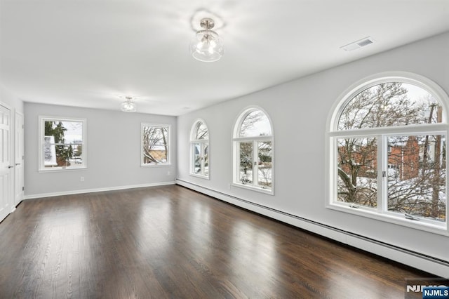 empty room featuring baseboard heating, plenty of natural light, and dark wood-type flooring