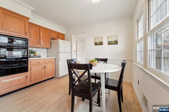 dining room featuring visible vents, baseboards, crown molding, and light wood-style floors