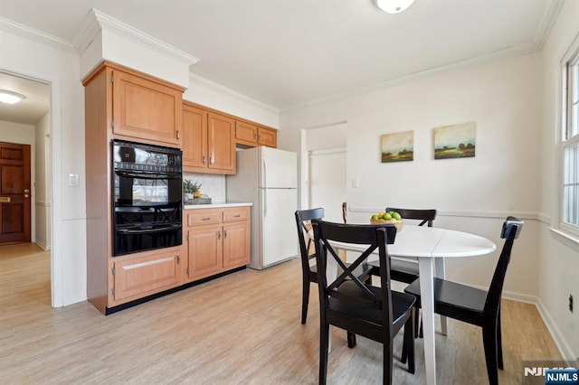 kitchen featuring black oven, ornamental molding, light wood-style flooring, freestanding refrigerator, and a warming drawer