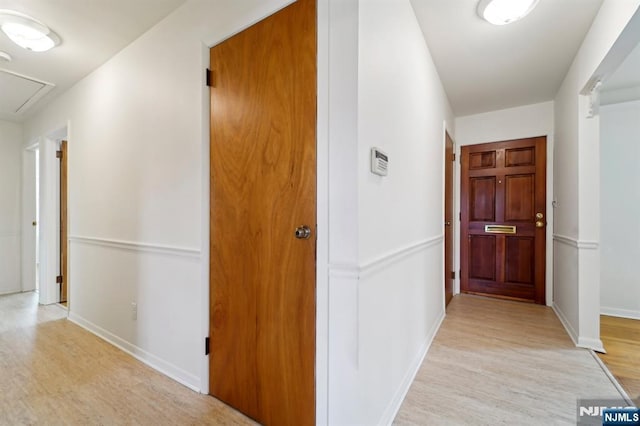 hallway featuring attic access, baseboards, and light wood finished floors