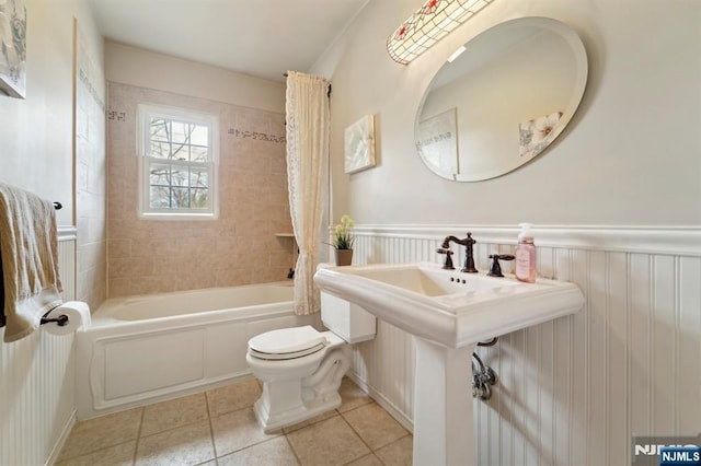 full bath with tile patterned floors, a wainscoted wall, toilet, and shower / tub combo