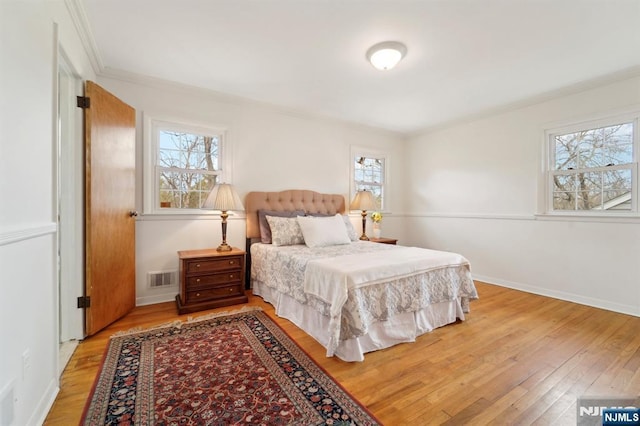 bedroom featuring light wood finished floors, visible vents, crown molding, and baseboards