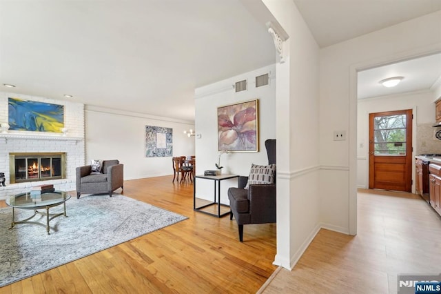 living room featuring visible vents, a brick fireplace, baseboards, and light wood-style floors