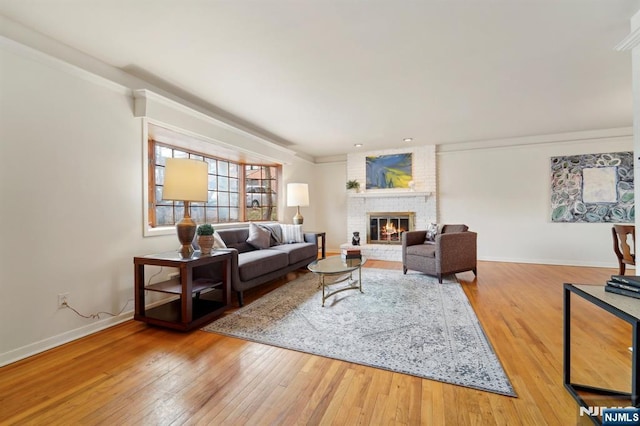 living area featuring a fireplace, crown molding, baseboards, and wood-type flooring