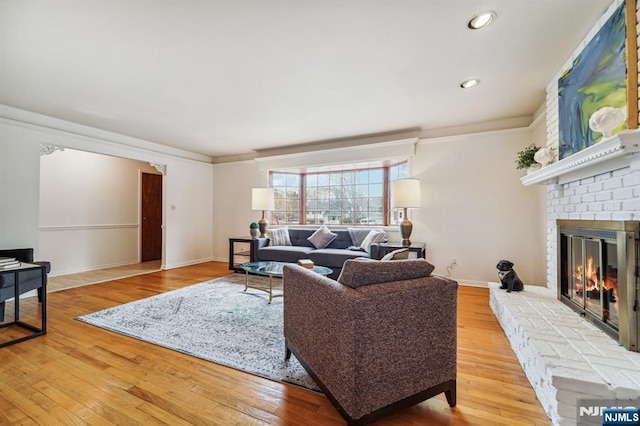 living area featuring crown molding, baseboards, recessed lighting, a fireplace, and wood-type flooring