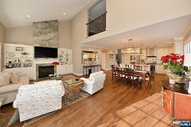 living room featuring a high ceiling, a chandelier, a fireplace, and light hardwood / wood-style flooring