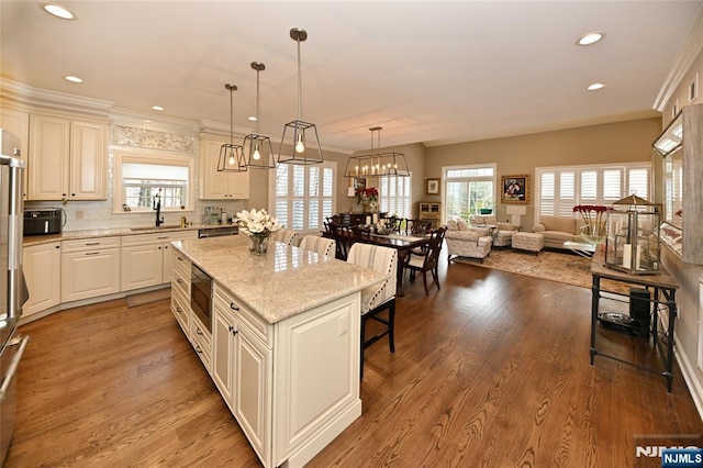 kitchen featuring sink, light stone counters, wood-type flooring, decorative light fixtures, and a kitchen island