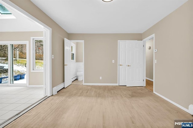 unfurnished bedroom with a baseboard radiator, ensuite bathroom, a skylight, and light hardwood / wood-style floors