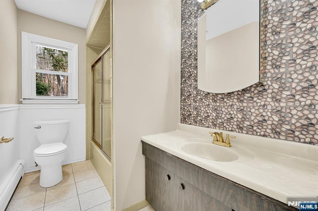 full bathroom featuring bath / shower combo with glass door, vanity, a baseboard heating unit, toilet, and tile patterned floors