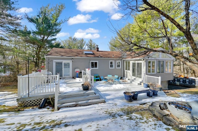 snow covered property with a wooden deck, a sunroom, and solar panels