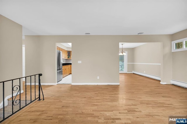 spare room featuring an inviting chandelier, light hardwood / wood-style floors, and baseboard heating